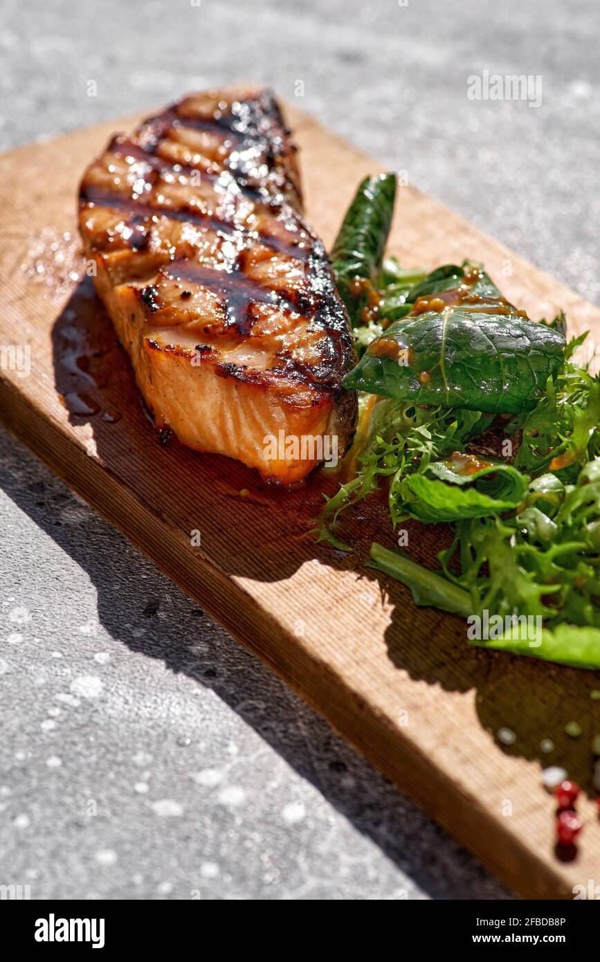 Macro shot of grilled salmon steak with bbq, fresh greens. Barbecue red trout fish fillet decorated with spicy greens on restaurant Stock Photo