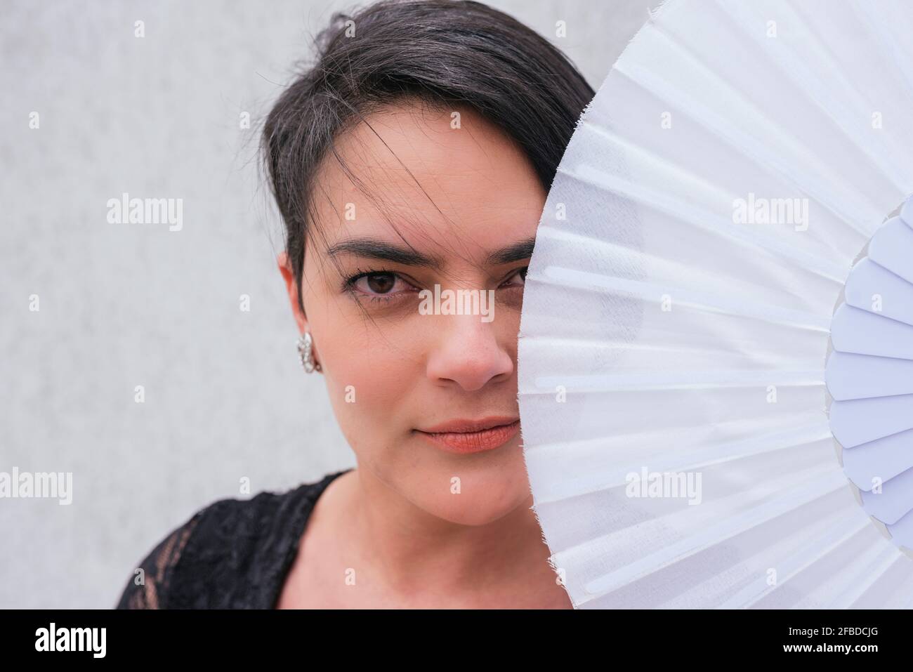 Caucasian woman covering face with hand fan in front of wall Stock Photo