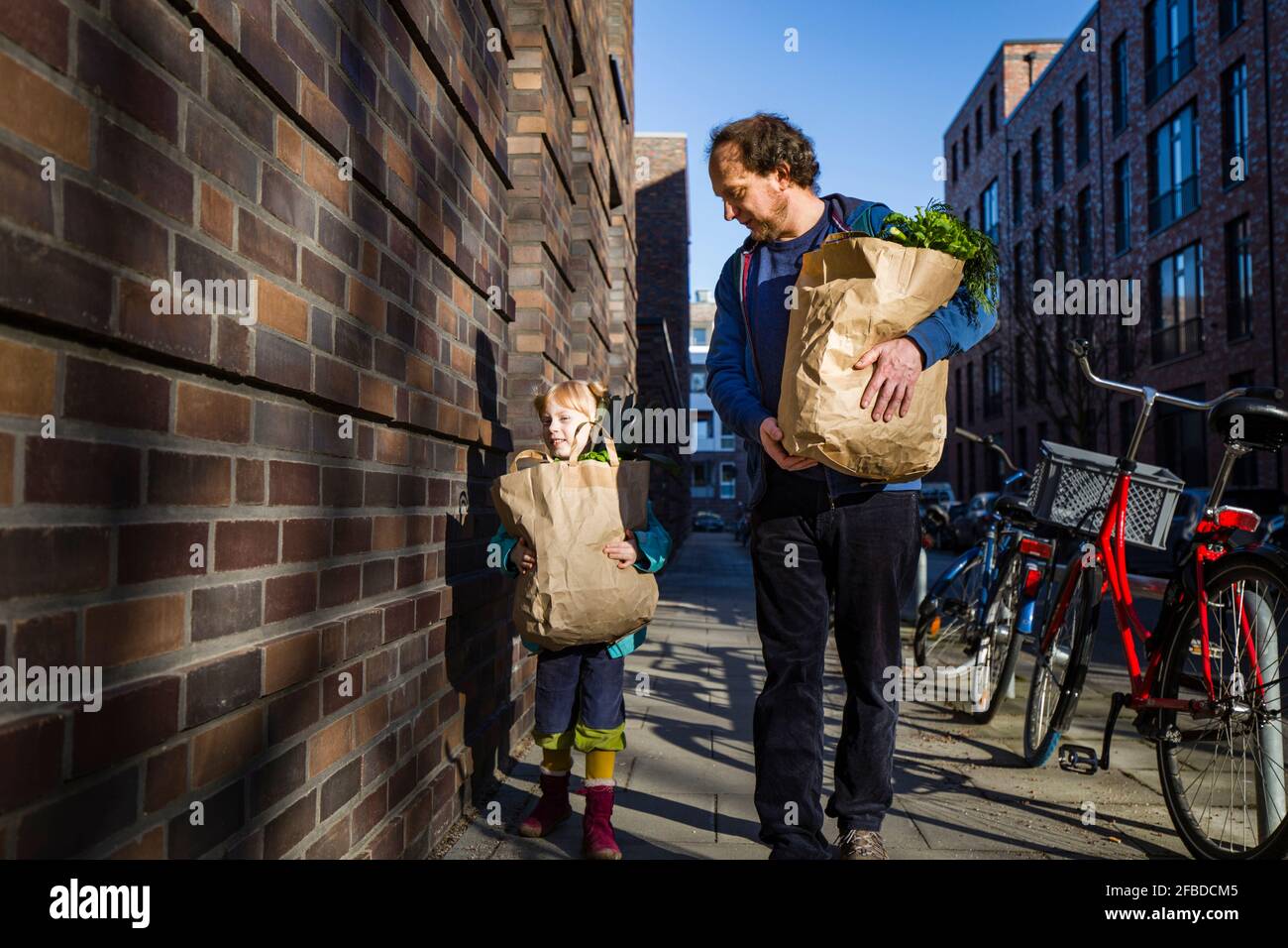 Man with daughter holding paper bag of vegetables while walking on alley Stock Photo