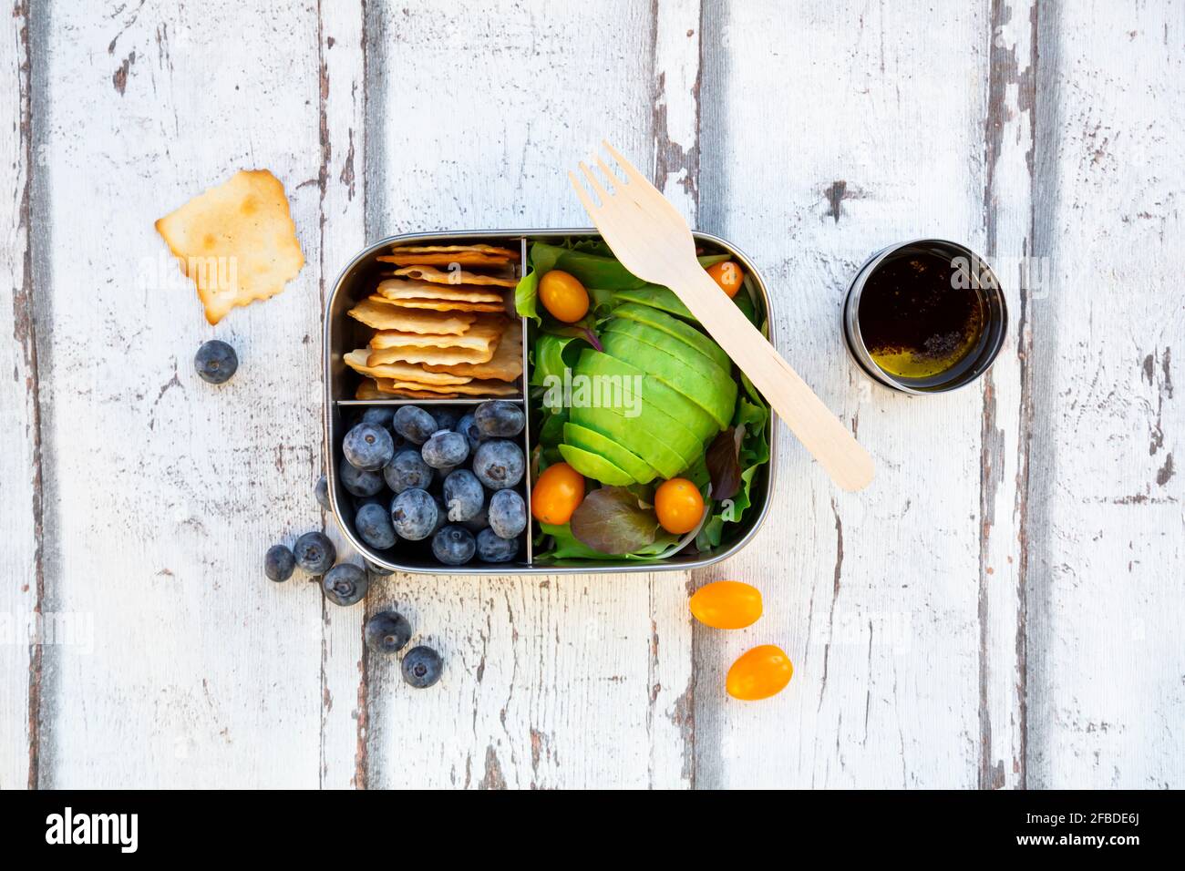 Lunchbox with salad, avocado and yellow tomatoes, crackers, blueberries and salad dressing Stock Photo