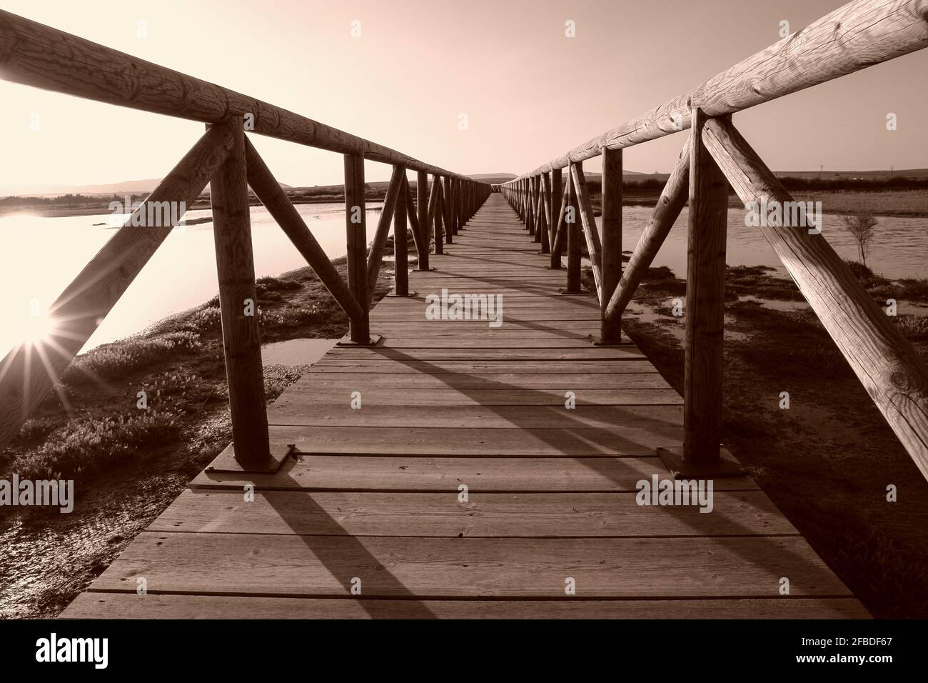 The sun's rays filter through a wooden bridge at the Laguna de Fuente de Piedra in Malaga. Stock Photo