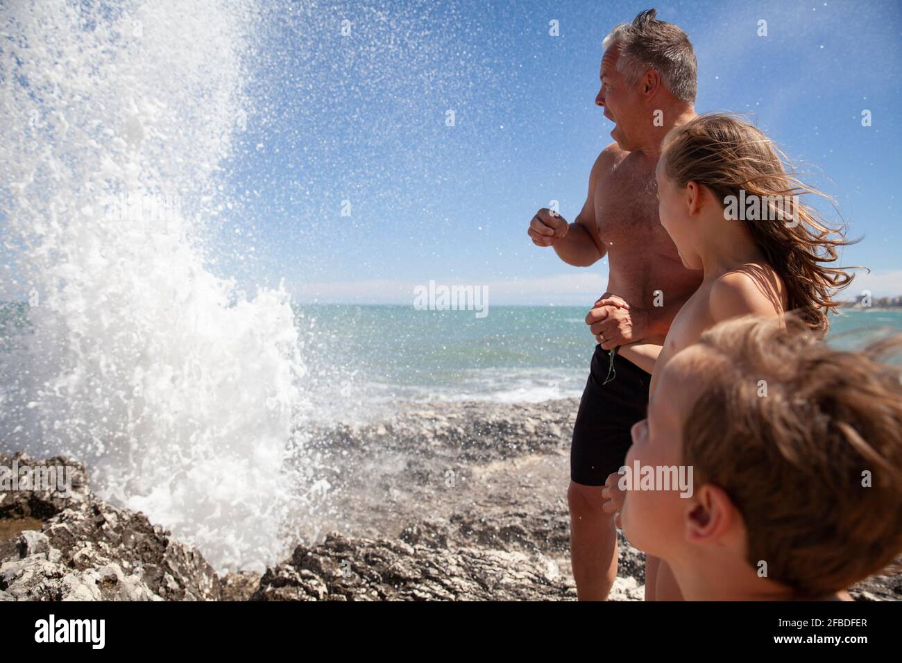 Father with children looking at water splash while standing on rock Stock Photo