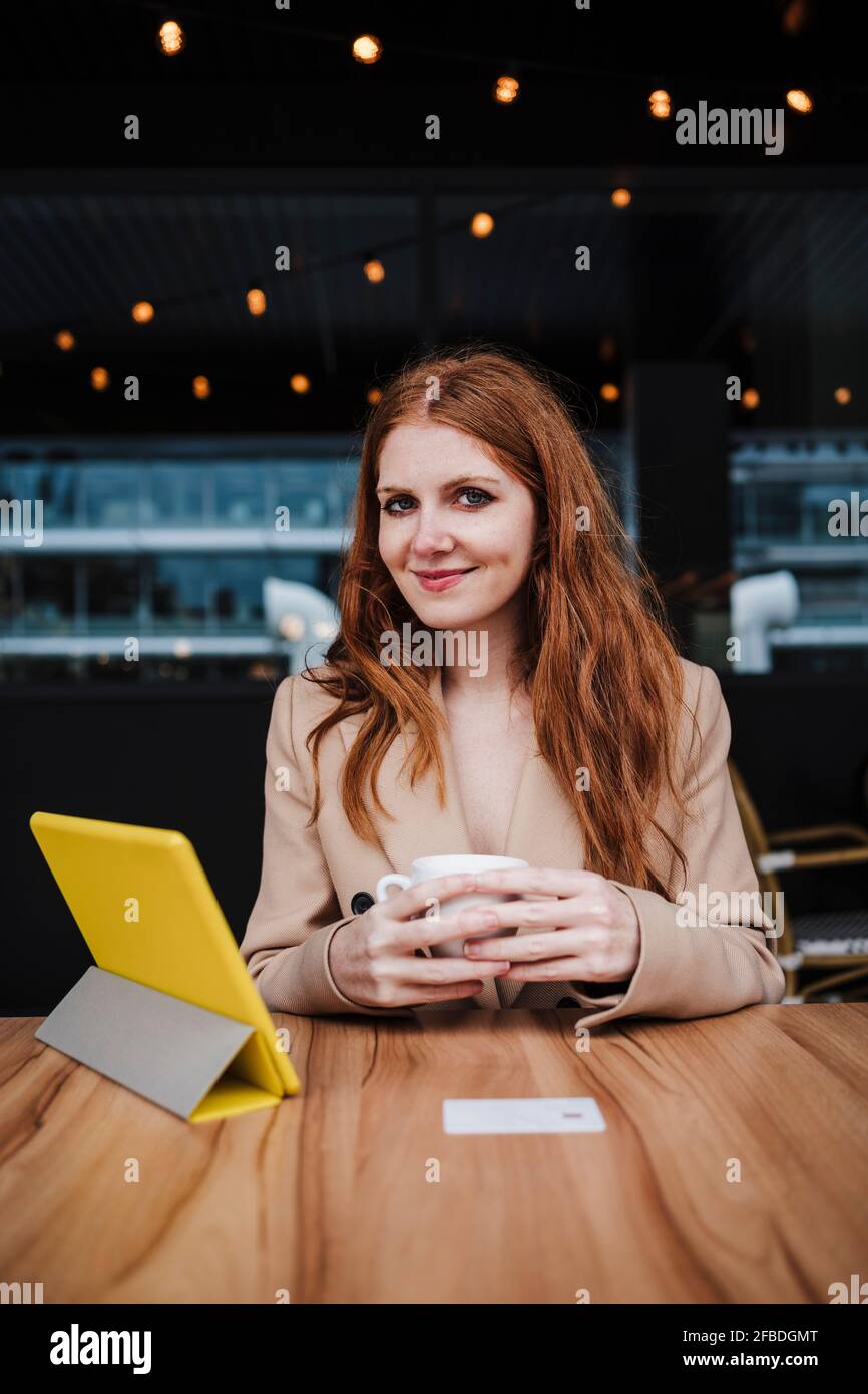 Smiling beautiful woman with red hair sitting at table in cafe Stock Photo