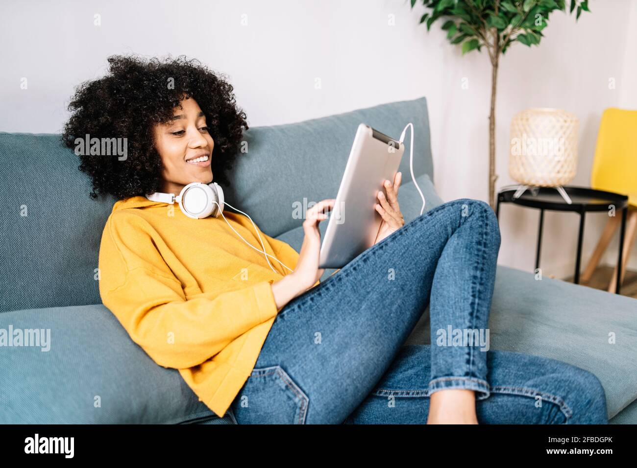 Relaxed young woman using digital tablet while sitting on sofa at home Stock Photo