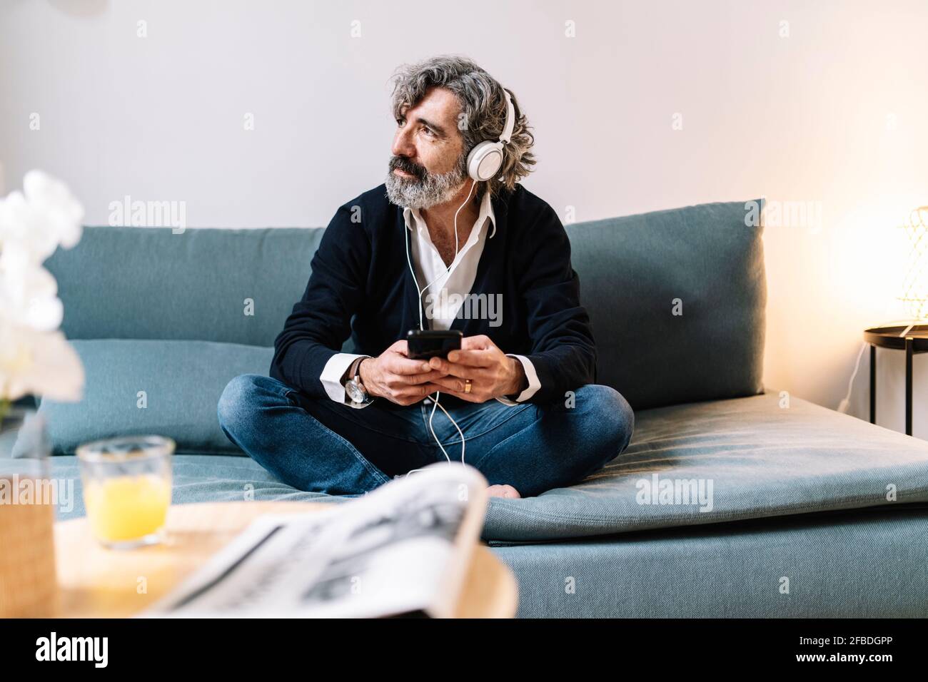 Thoughtful senior man looking away while using smart phone at home Stock Photo