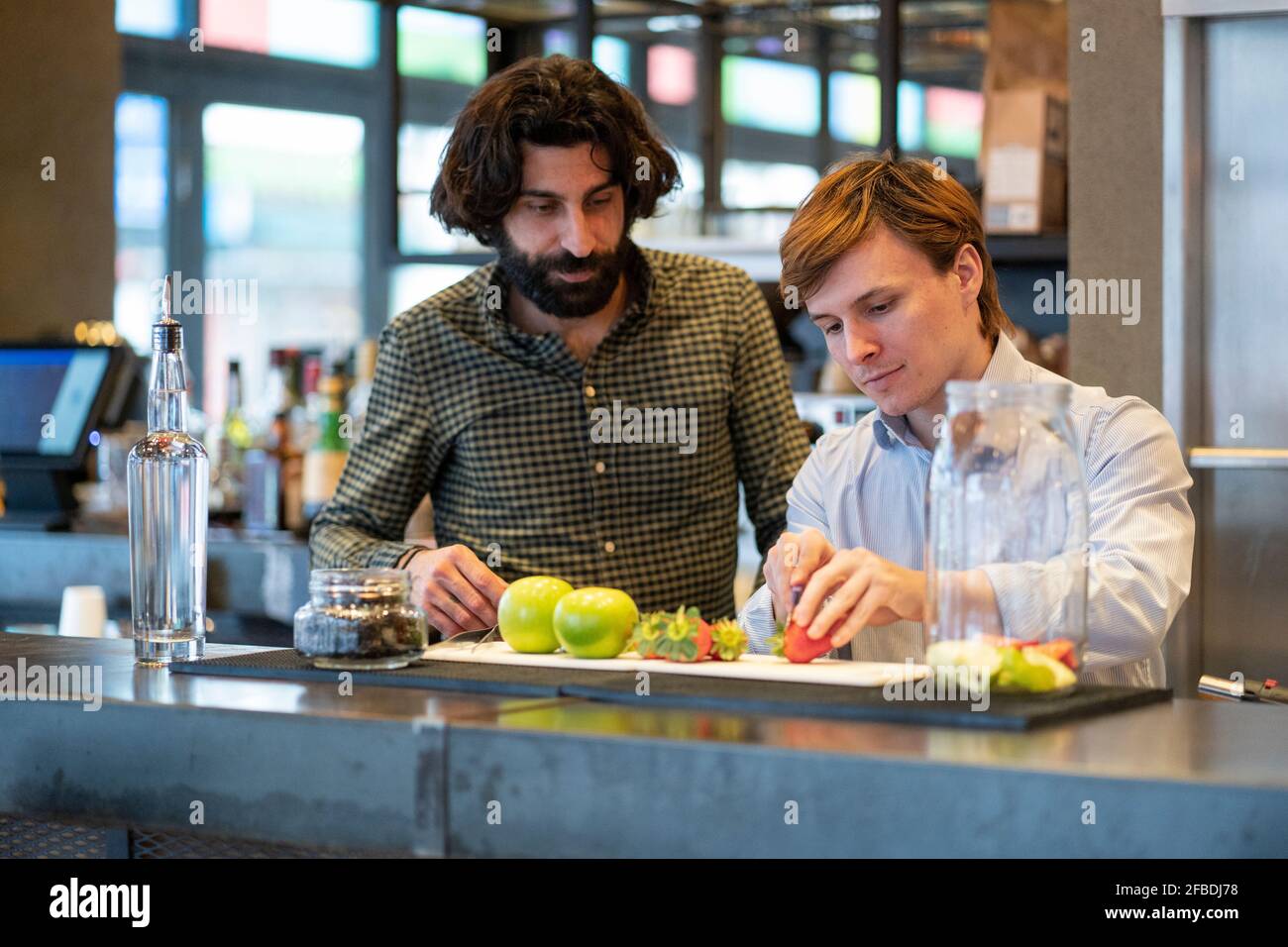Bartender looking at trainee cutting strawberry at bar counter Stock Photo