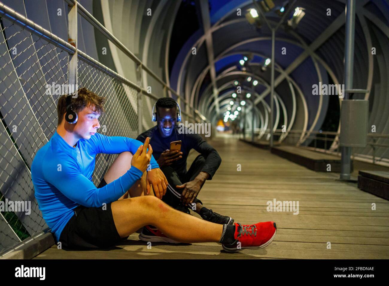 Young athletes using smart phones while relaxing on footbridge Stock Photo
