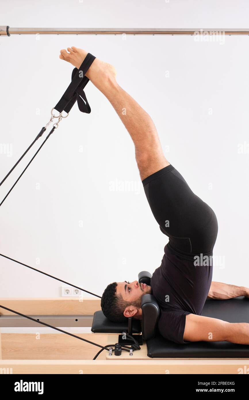 https://c8.alamy.com/comp/2FBE0XG/male-athlete-with-legs-raised-practicing-pilates-on-cadillac-reformer-in-exercise-room-2FBE0XG.jpg