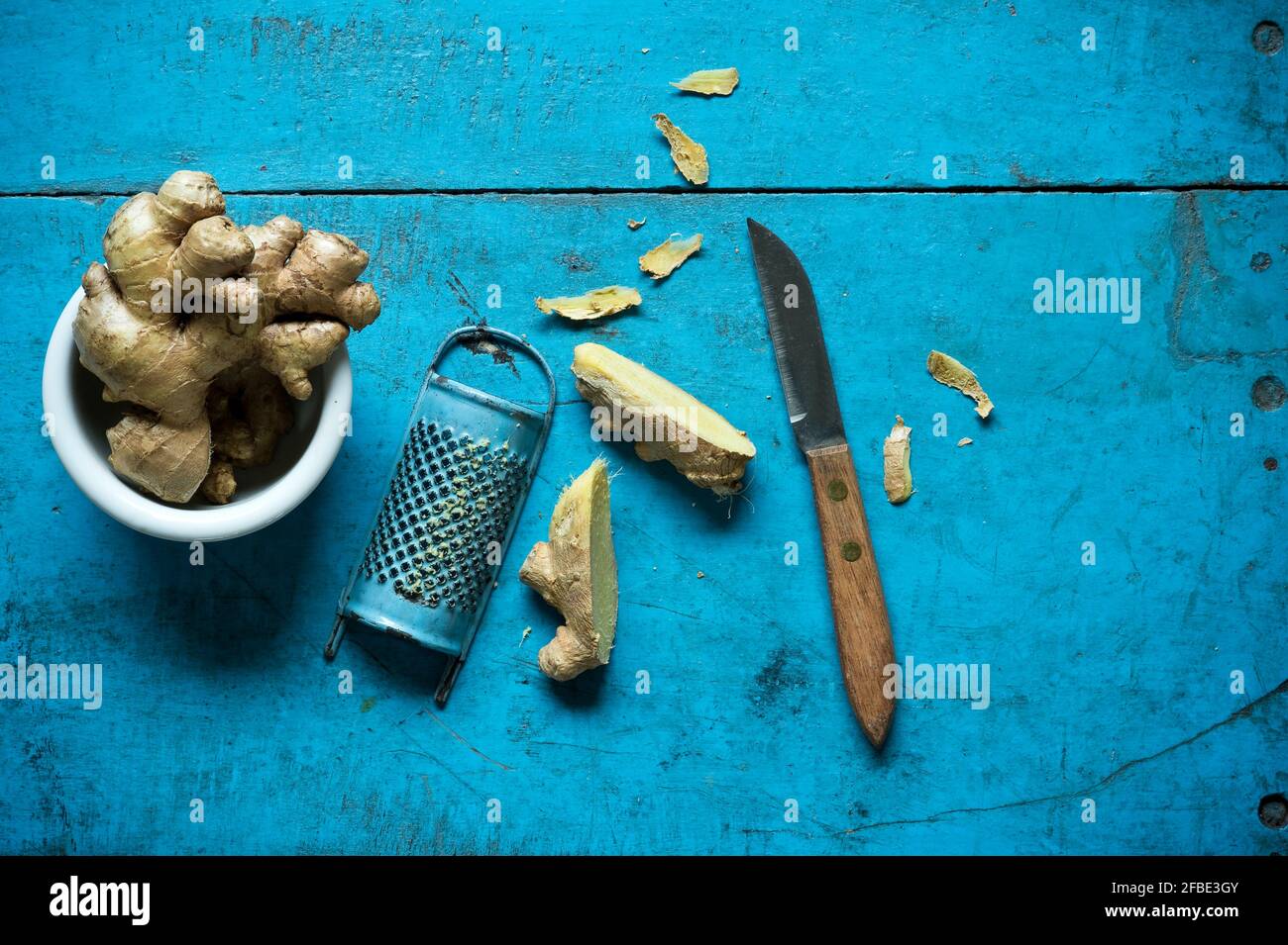 Ginger root, grater and kitchen knife lying on blue wooden surface