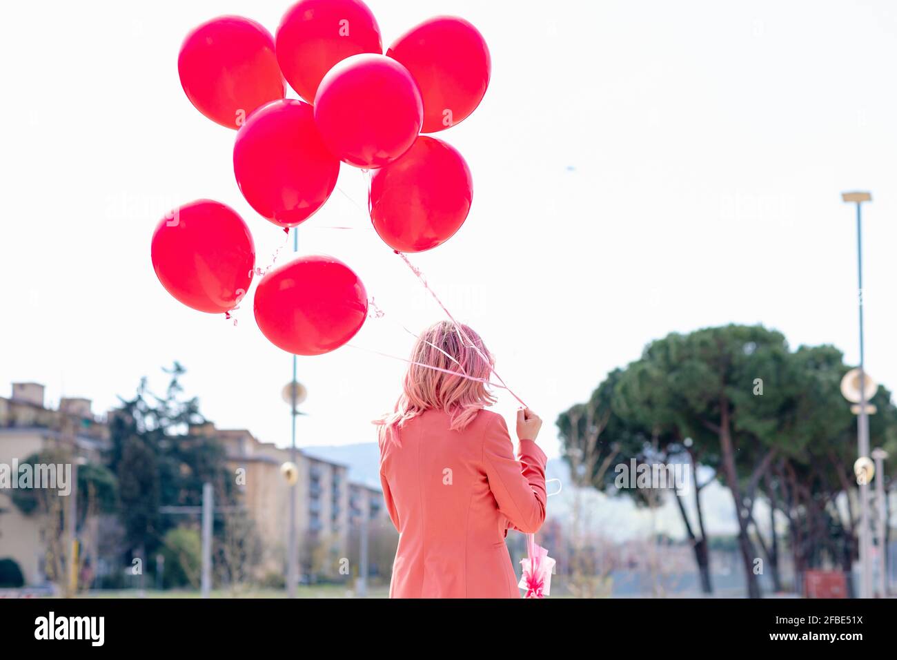 Woman in smart casual holding bunch of pink balloons Stock Photo