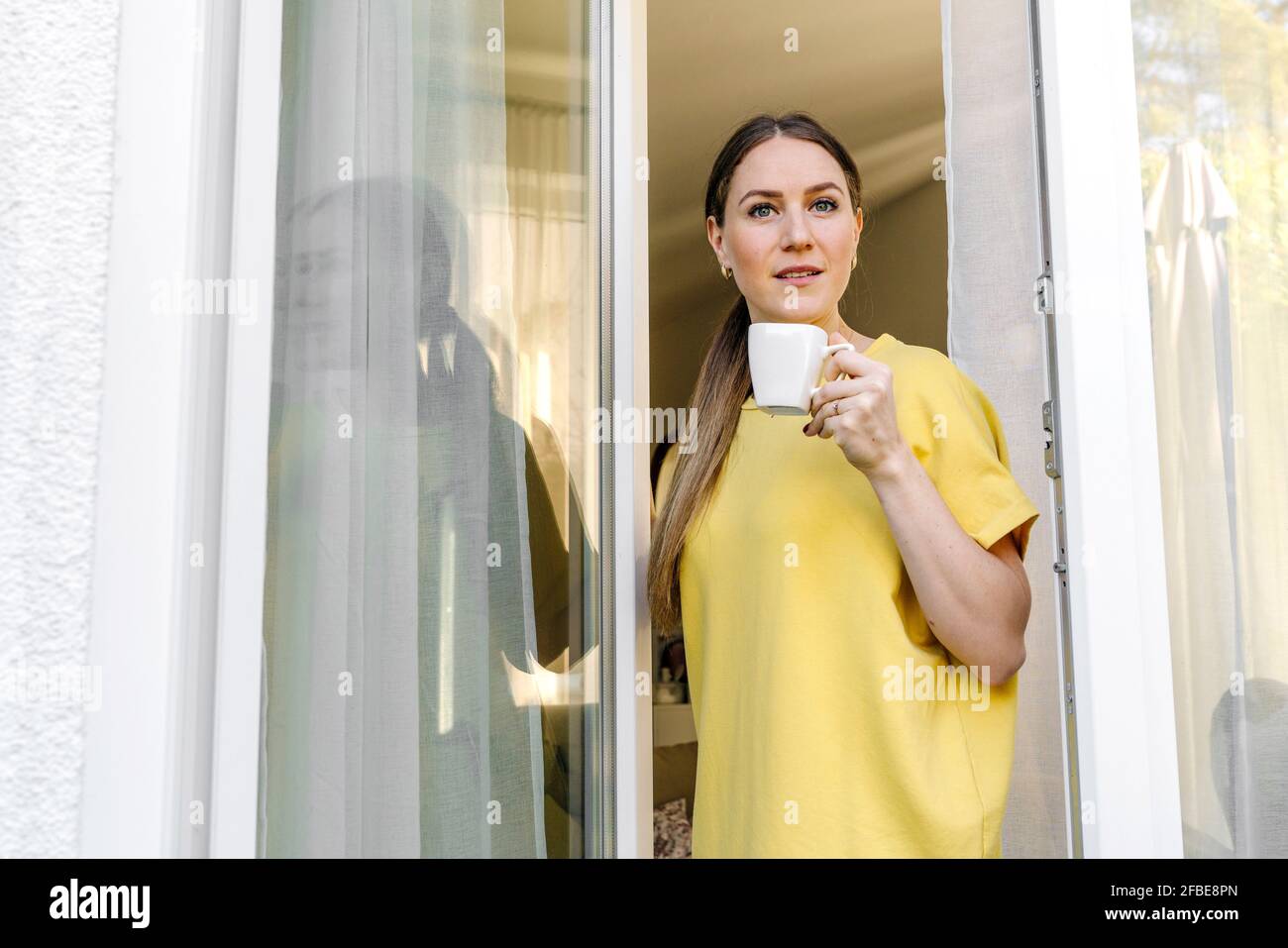 Brown haired woman with coffee cup standing at window Stock Photo