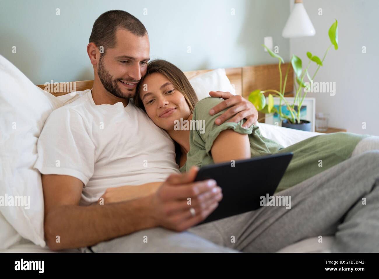 Smiling young couple using digital tablet while lying on bed at home Stock Photo