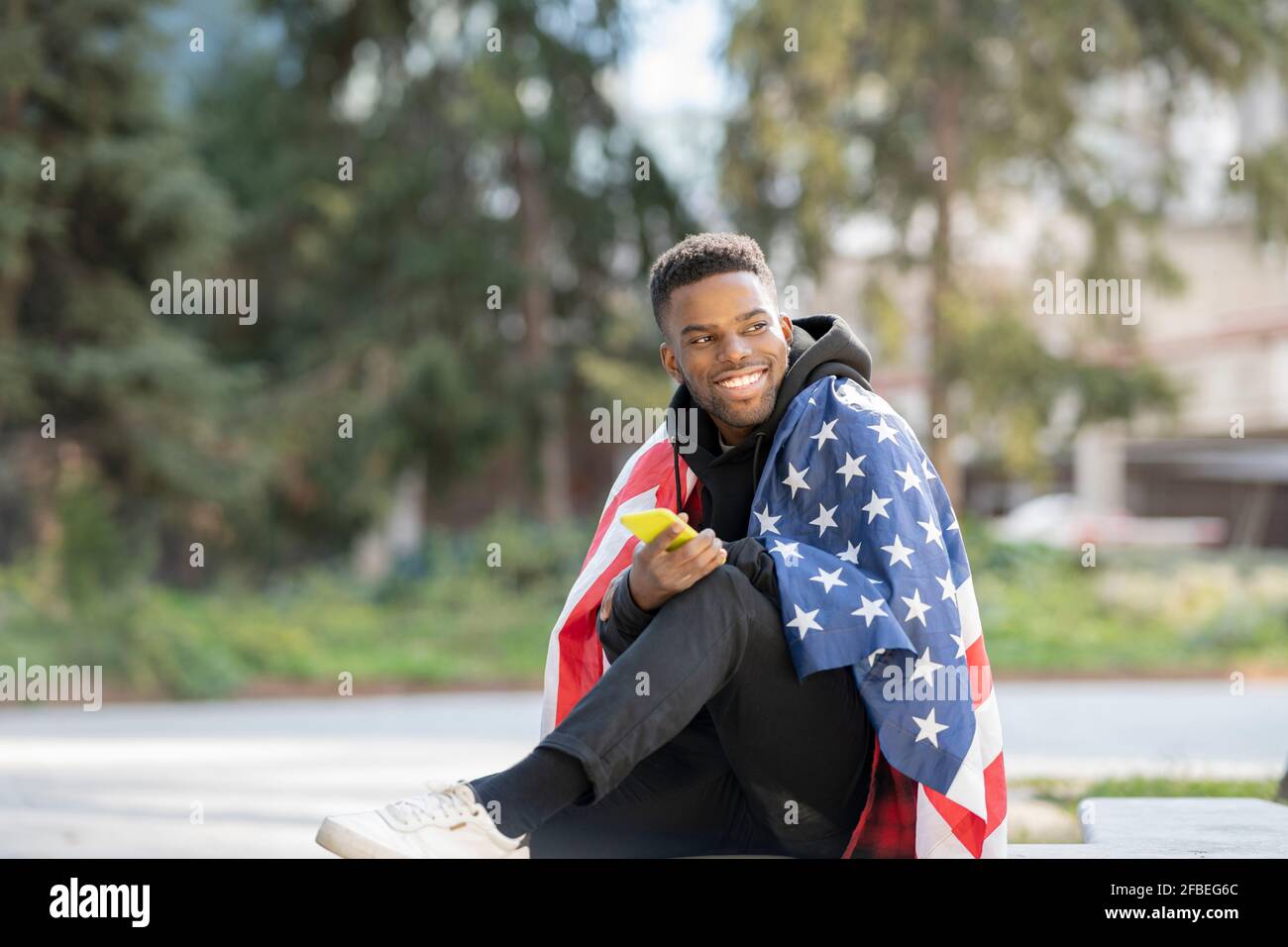 Young man wrapped in American Flag while looking away at park Stock Photo