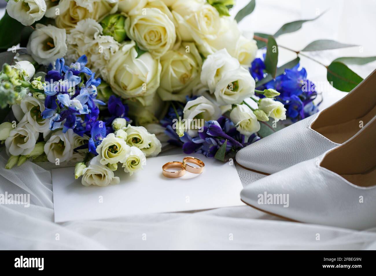 Wedding shoes for the bride. White high-heeled shoes near wedding rings, wedding jewelry. Marriage concept Stock Photo