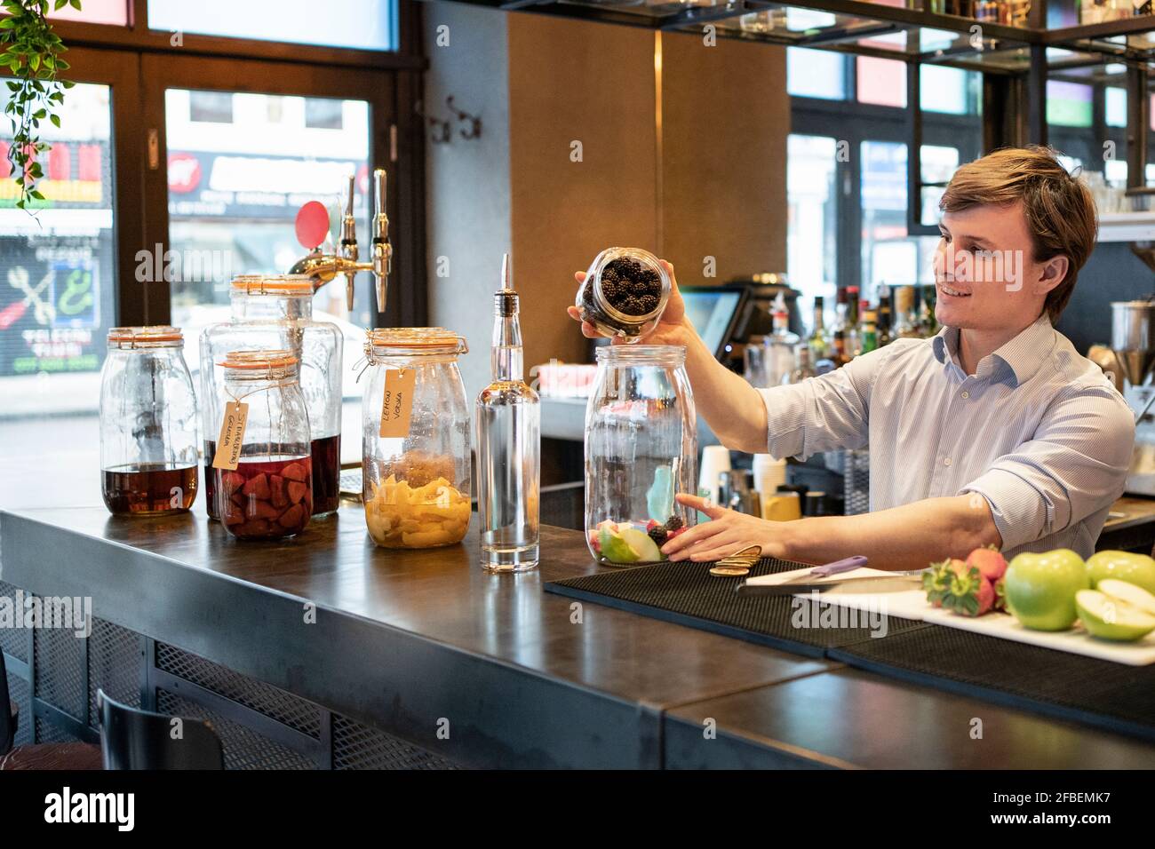 Male trainee putting blackberries in glass jar at bar counter Stock Photo