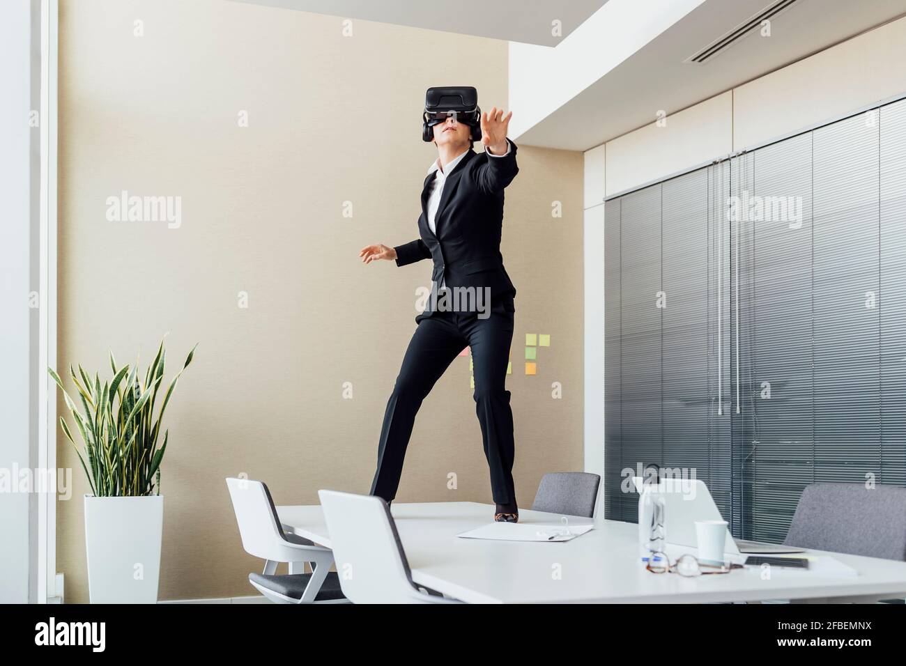 Female using virtual reality headset while standing on conference table in office Stock Photo