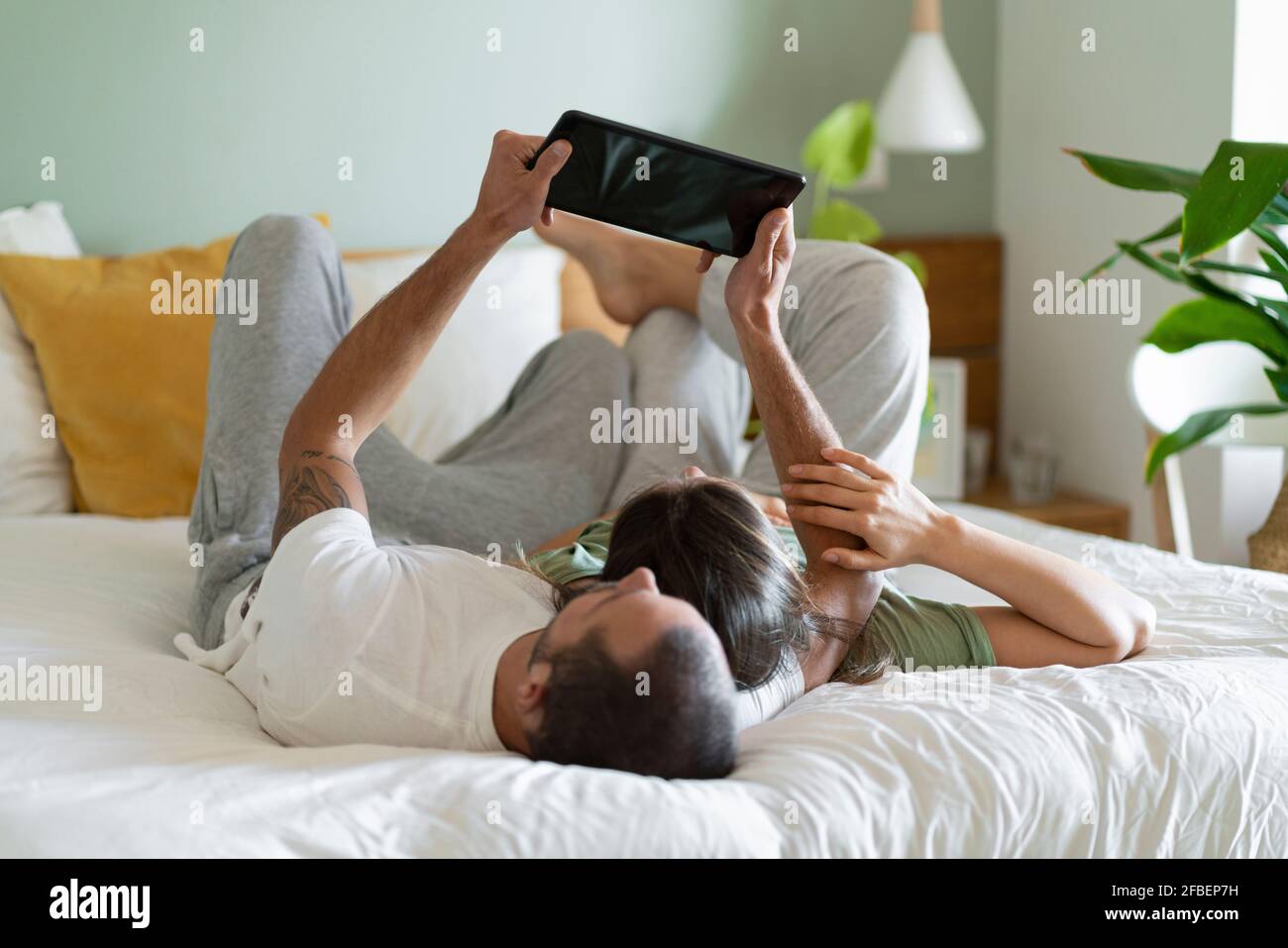 Relaxed young couple using digital tablet while lying on bed at home Stock Photo