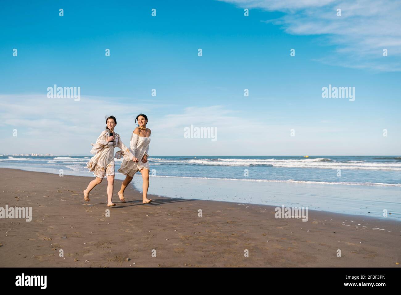 Female friends looking away while running by water at beach Stock Photo
