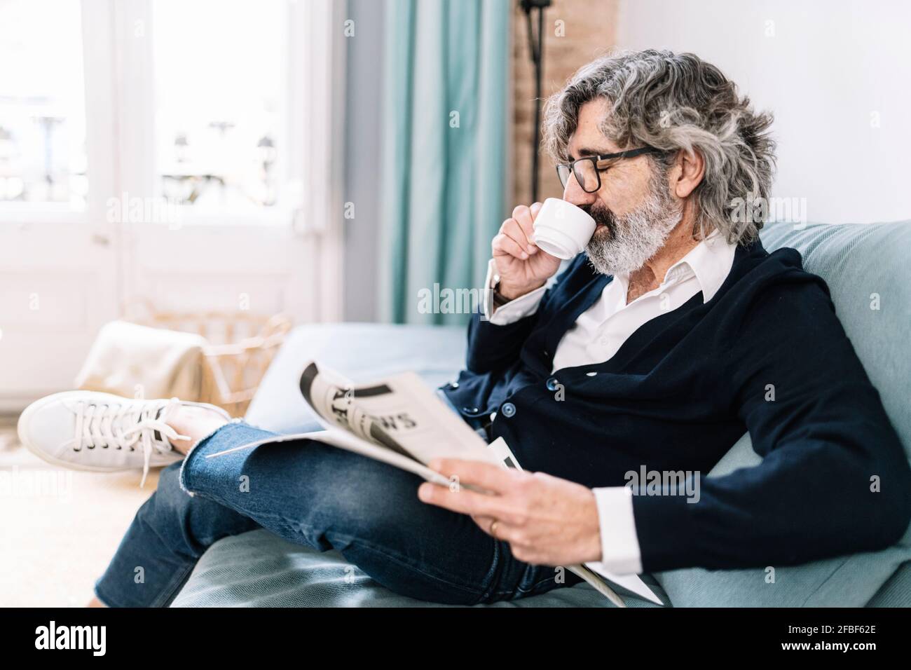 Man holding newspaper having coffee while sitting on sofa at home Stock Photo