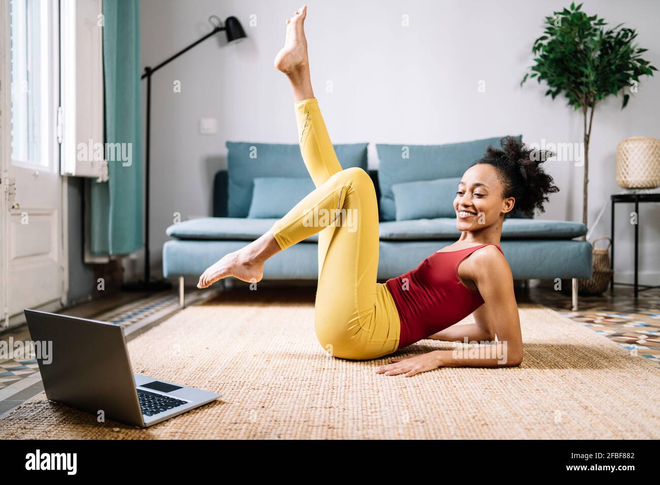 Smiling young woman exercising while watching tutorial on laptop at home Stock Photo