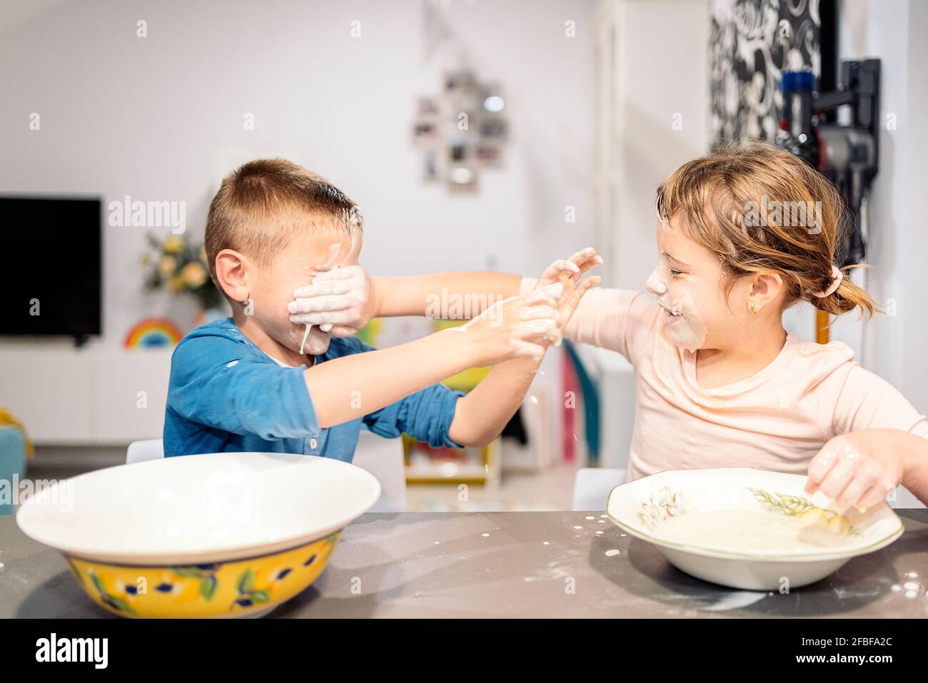 Playful siblings smearing faces with flour and water at home Stock Photo