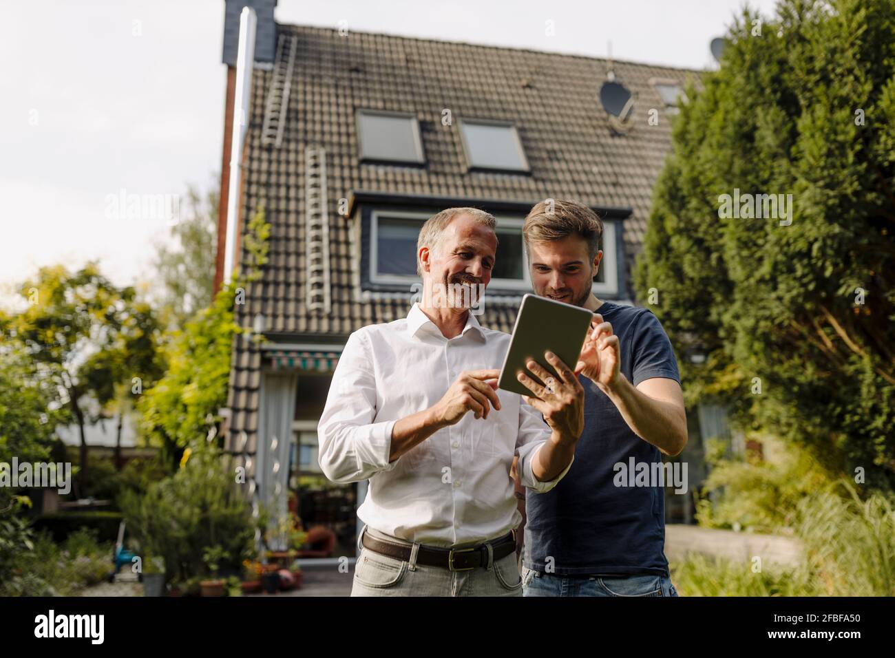 Happy father and son using digital tablet while standing in backyard Stock Photo
