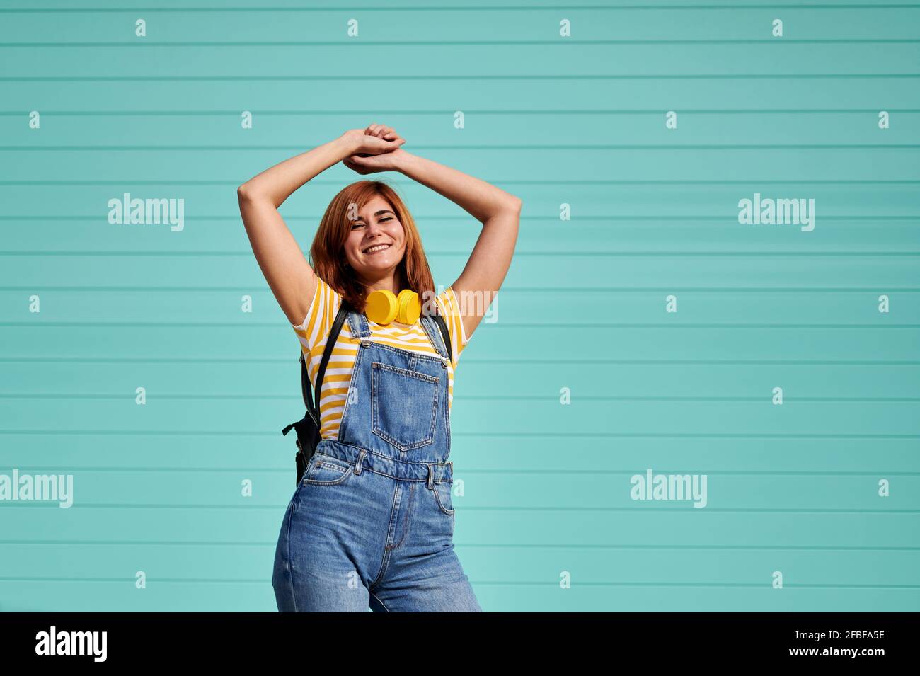 Smiling woman dancing in front of turquoise blue wall Stock Photo