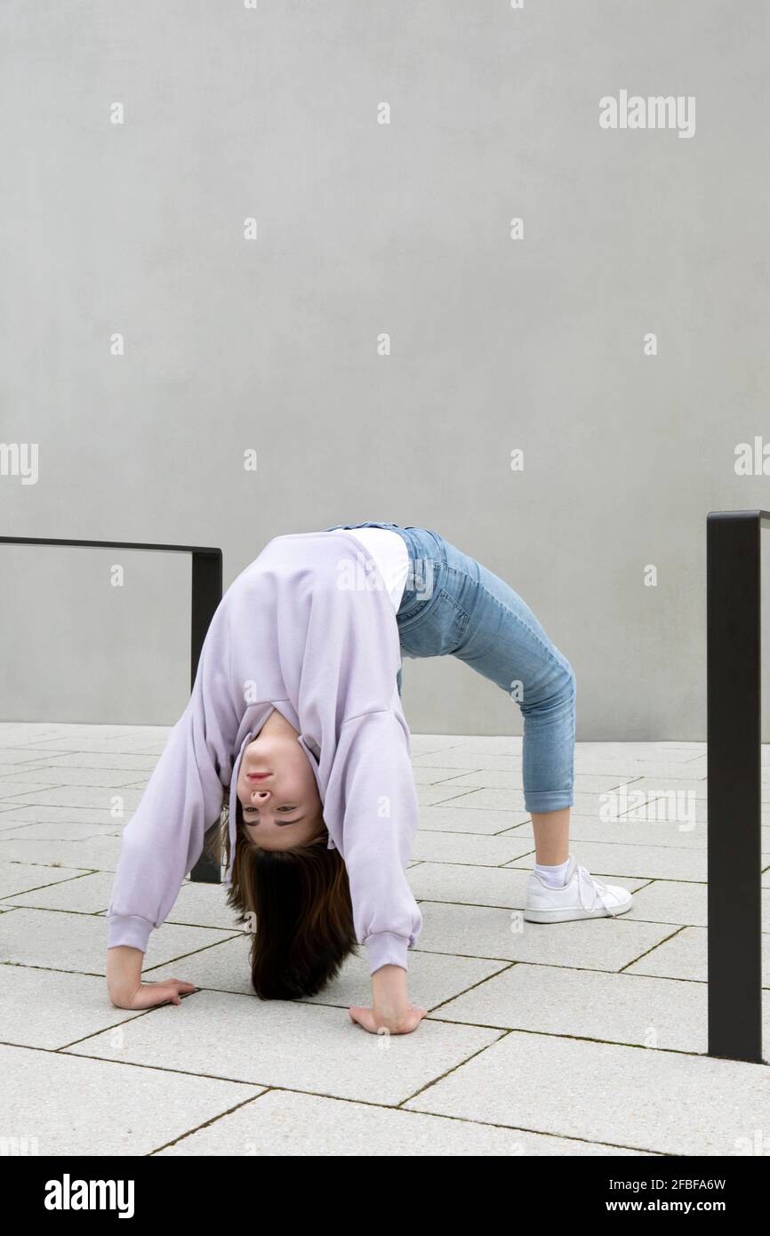 Girl bending over backwards by wall Stock Photo