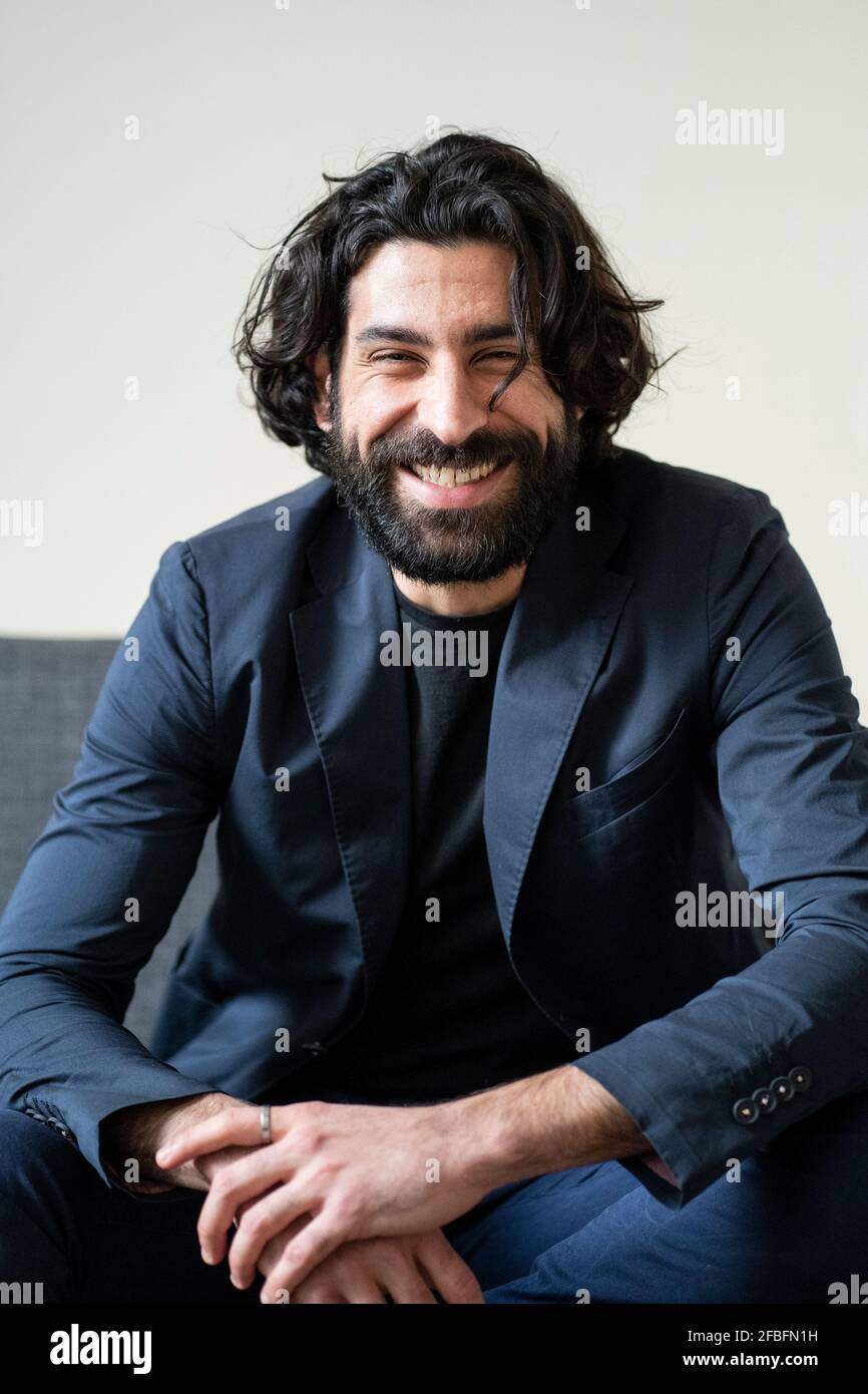 Bearded man smiling while sitting on sofa Stock Photo