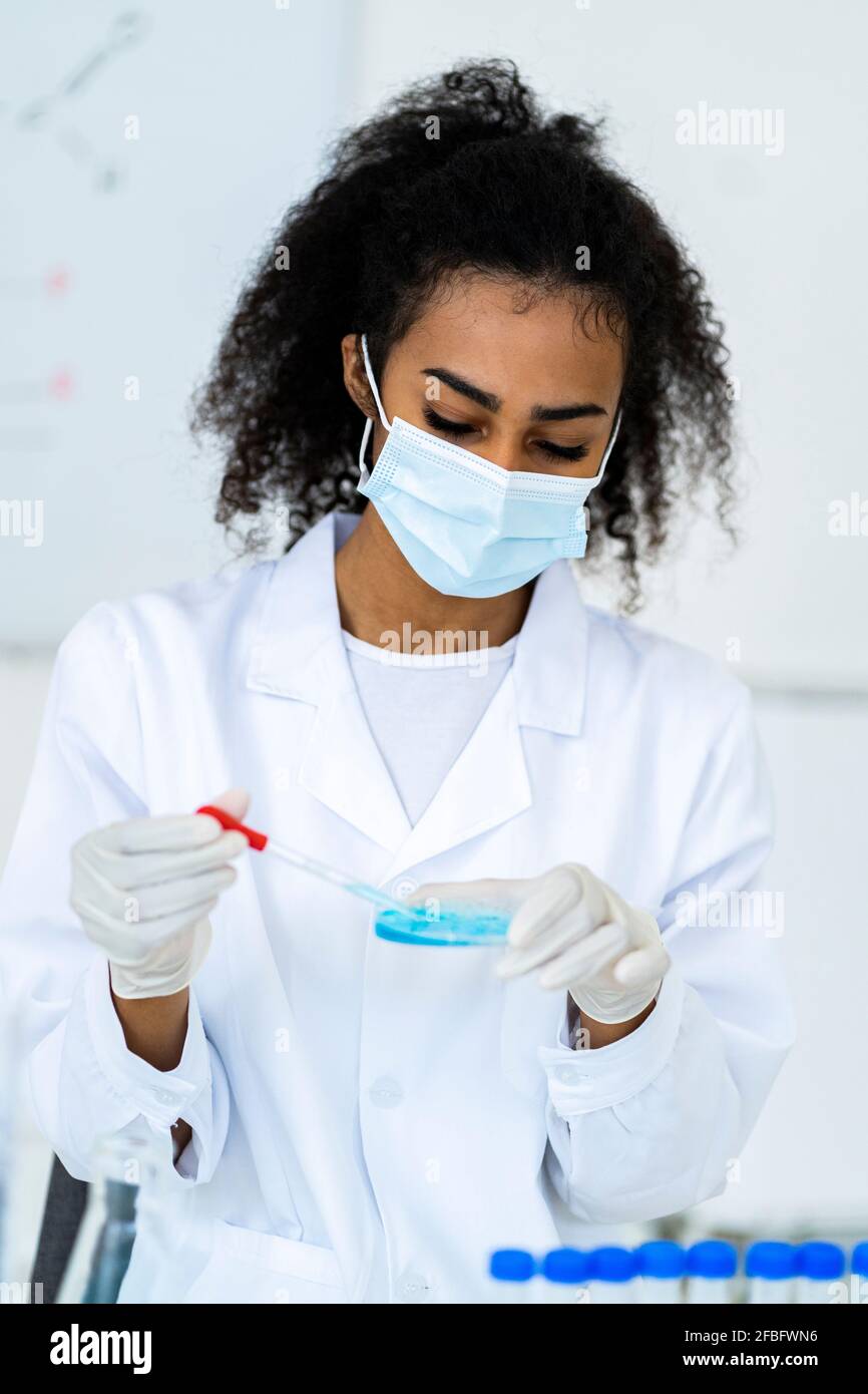 Young female researcher testing liquid in chemistry laboratory during COVID-19 Stock Photo