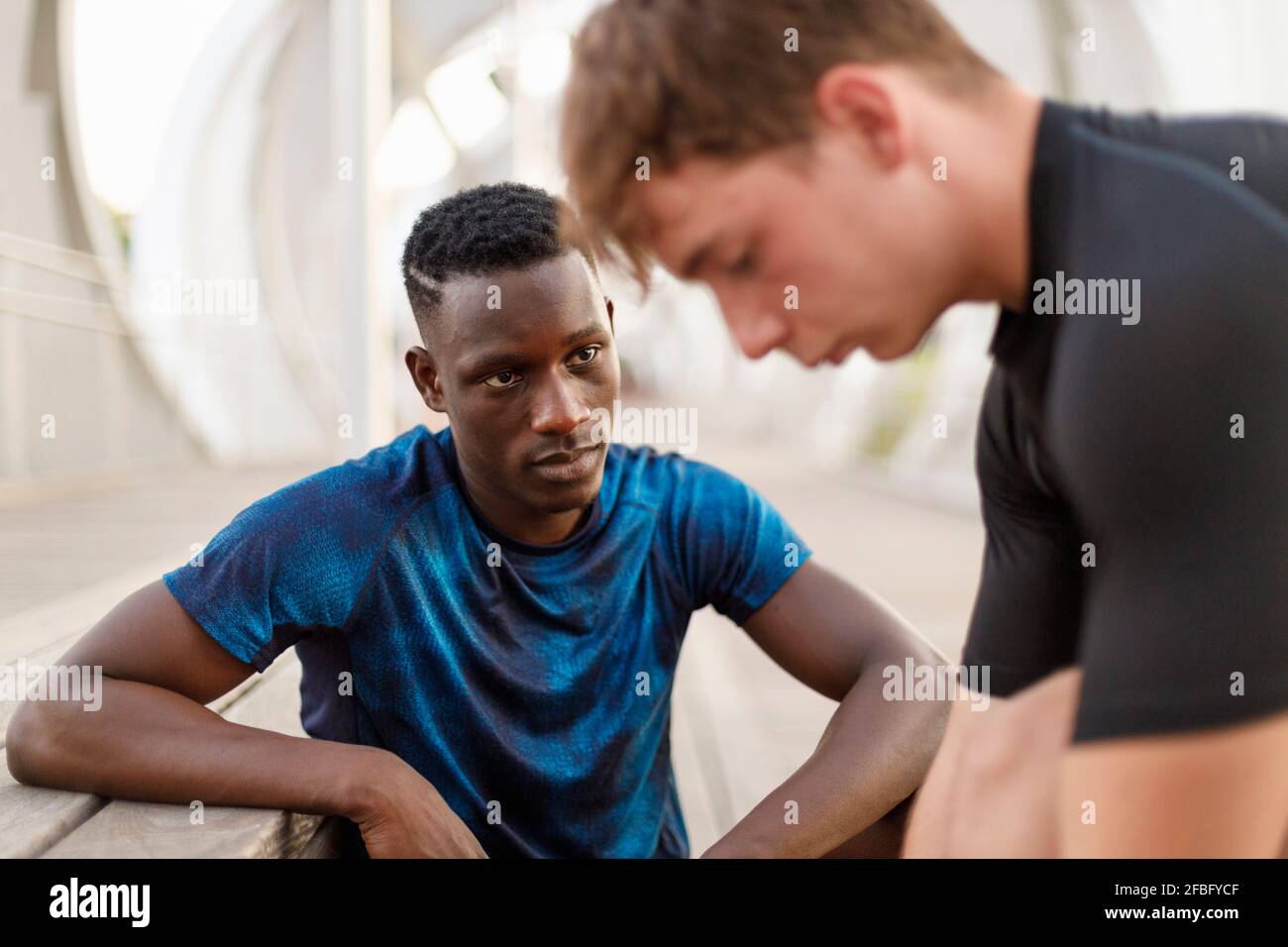 Young man looking while friend tying shoelace on wooden seat Stock Photo