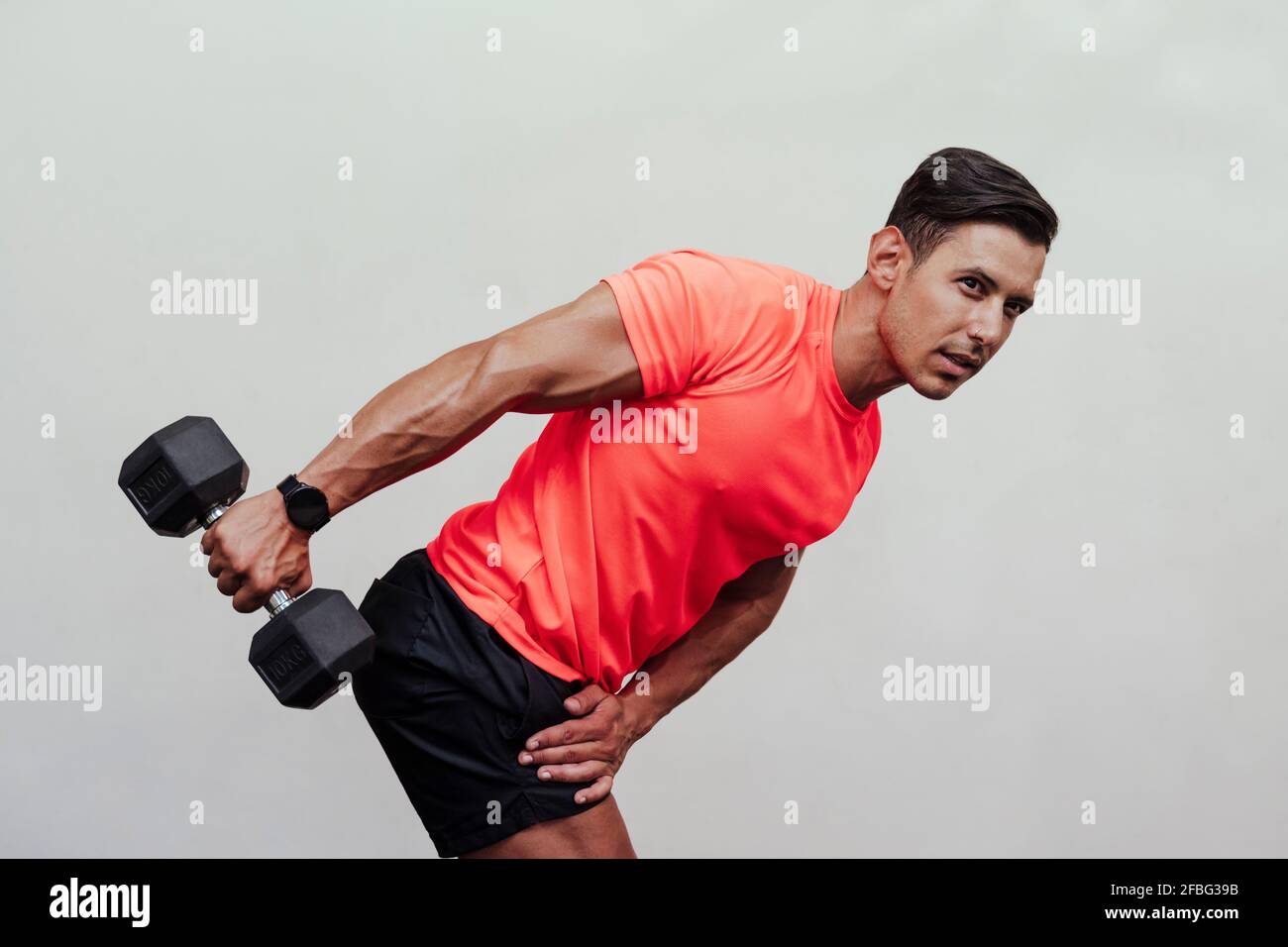 Male sportsperson bending while exercising with dumbbell by white wall Stock Photo