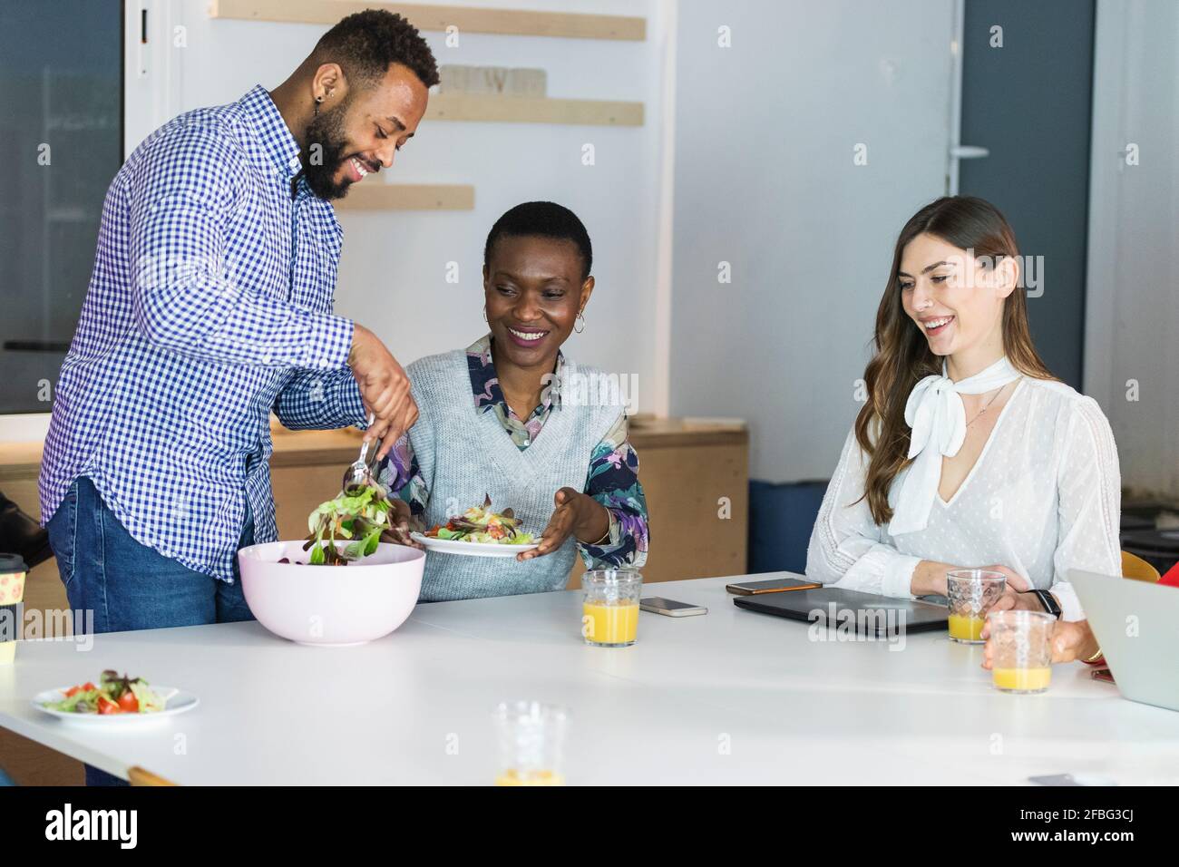 Male colleague serving meal to businesswomen at cafeteria Stock Photo