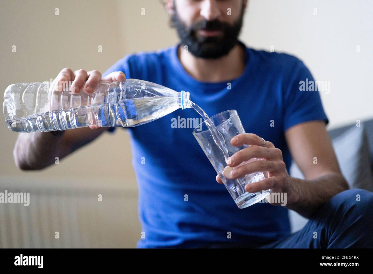 Thirsty young man pouring water in drinking glass at home Stock Photo