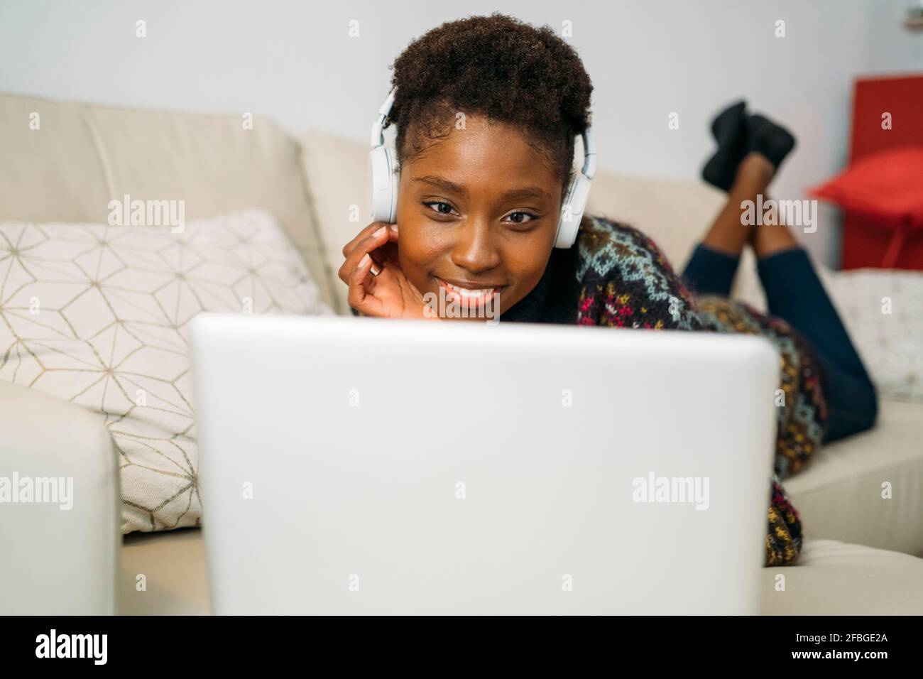 Young female entrepreneur with headphones teleworking through laptop in living room Stock Photo