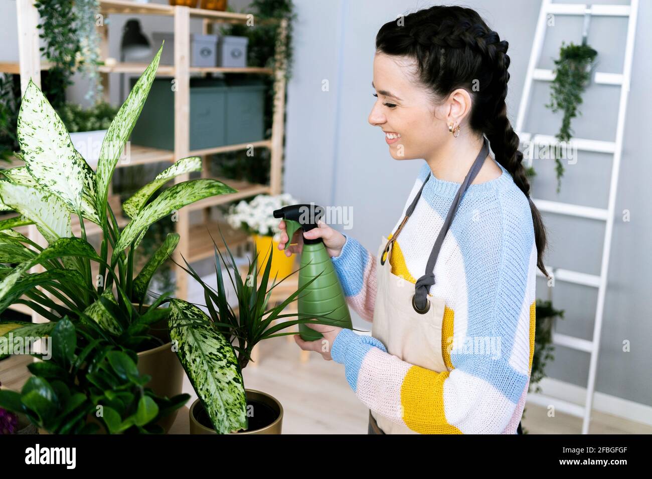 Smiling woman spraying water on plants while working at workshop Stock Photo