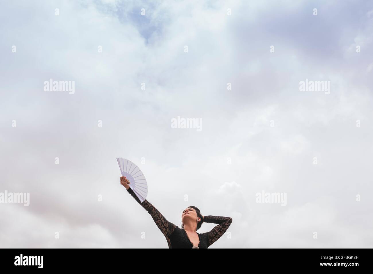 Female dancer with hand fan performing flamenco under cloudy sky Stock Photo