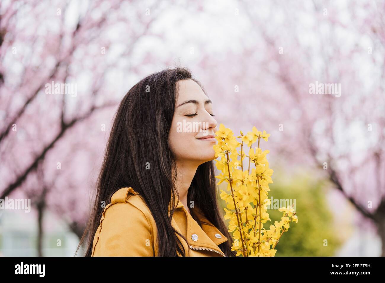 Smiling woman with eyes closed smelling fragrance of yellow flowers ...