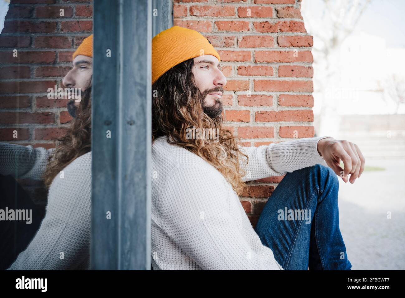 Man wearing knit hat sitting by brick wall while looking away Stock Photo