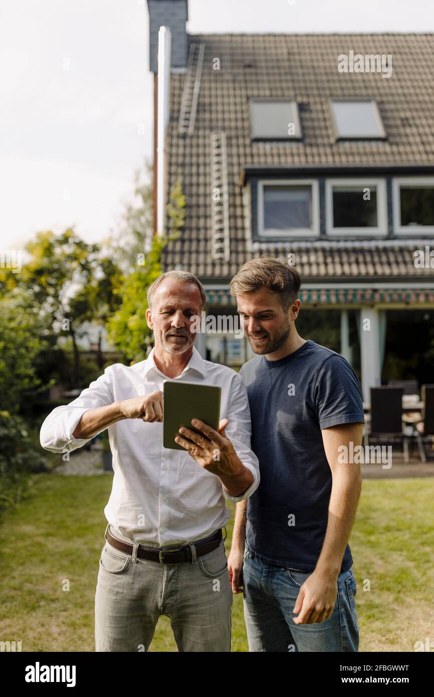 Father using digital tablet while standing by son in backyard Stock Photo