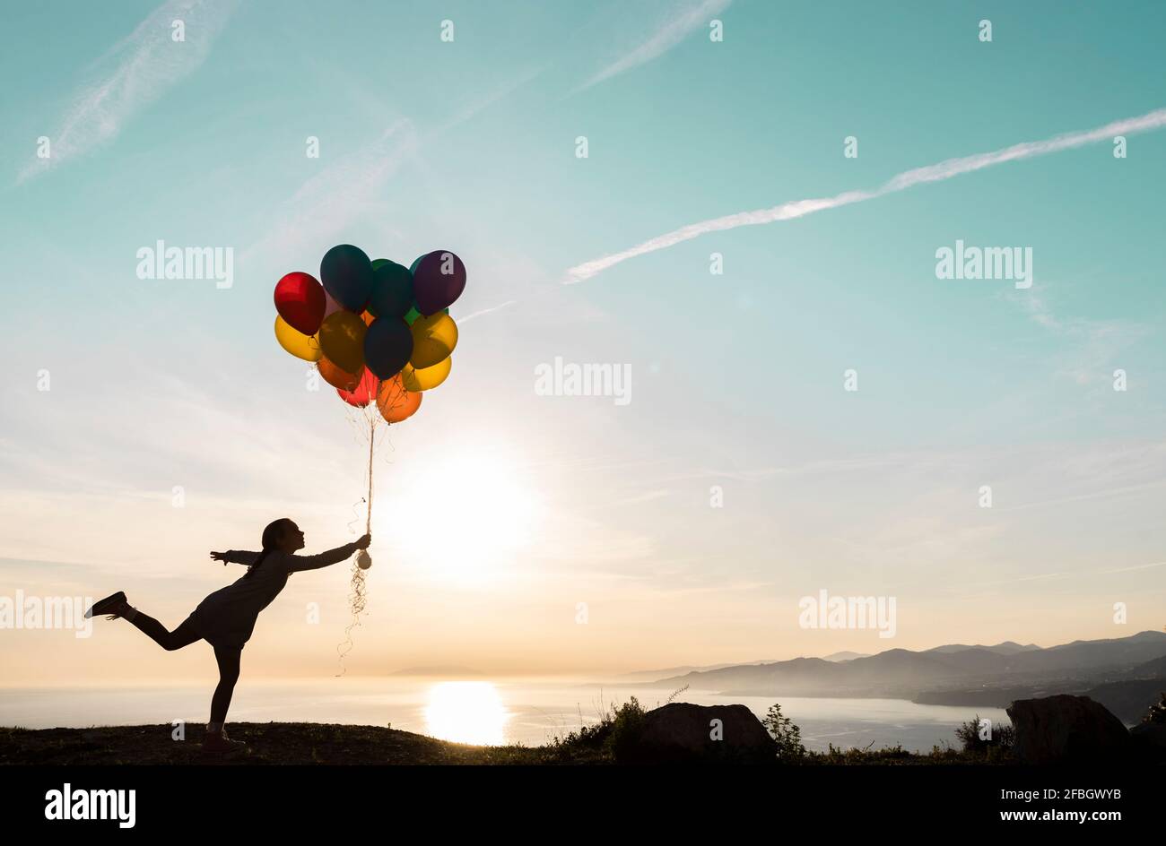 Girl in silhouette playing with balloons during sunset Stock Photo