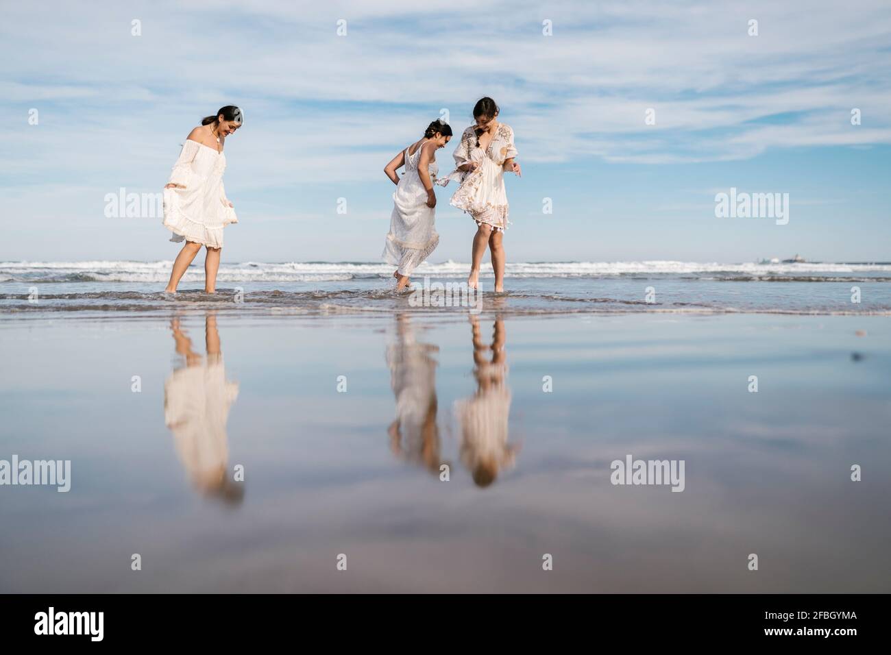 Female friends having fun while walking in water at beach Stock Photo