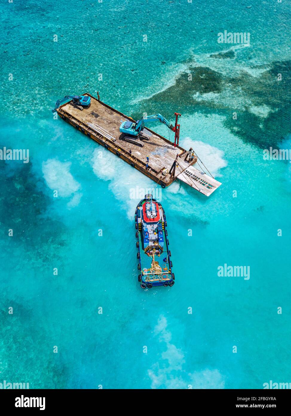 Aerial view of earth movers handling poles on floating platform in Male