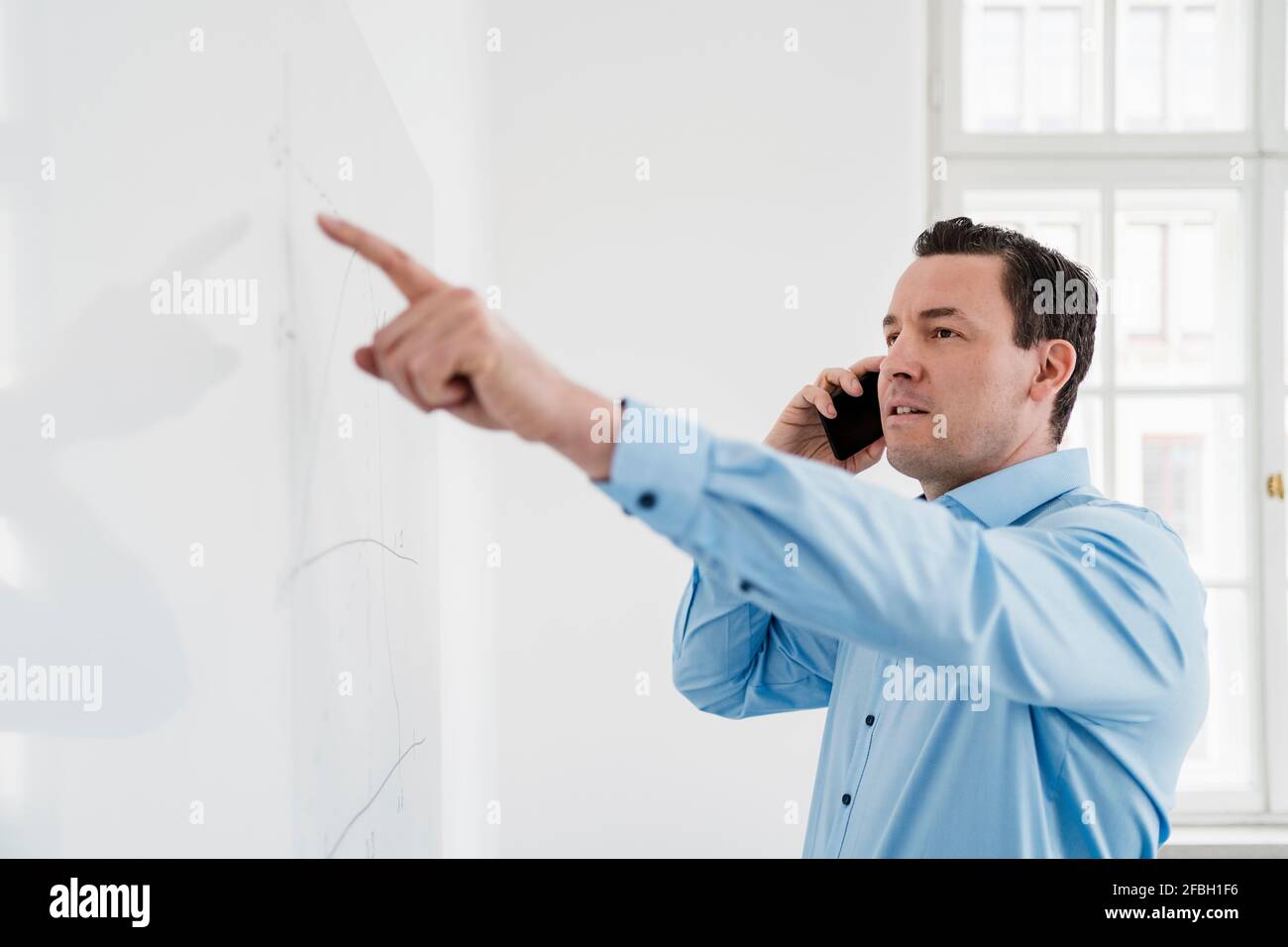 Male entrepreneur talking on phone while analyzing chart at office Stock Photo