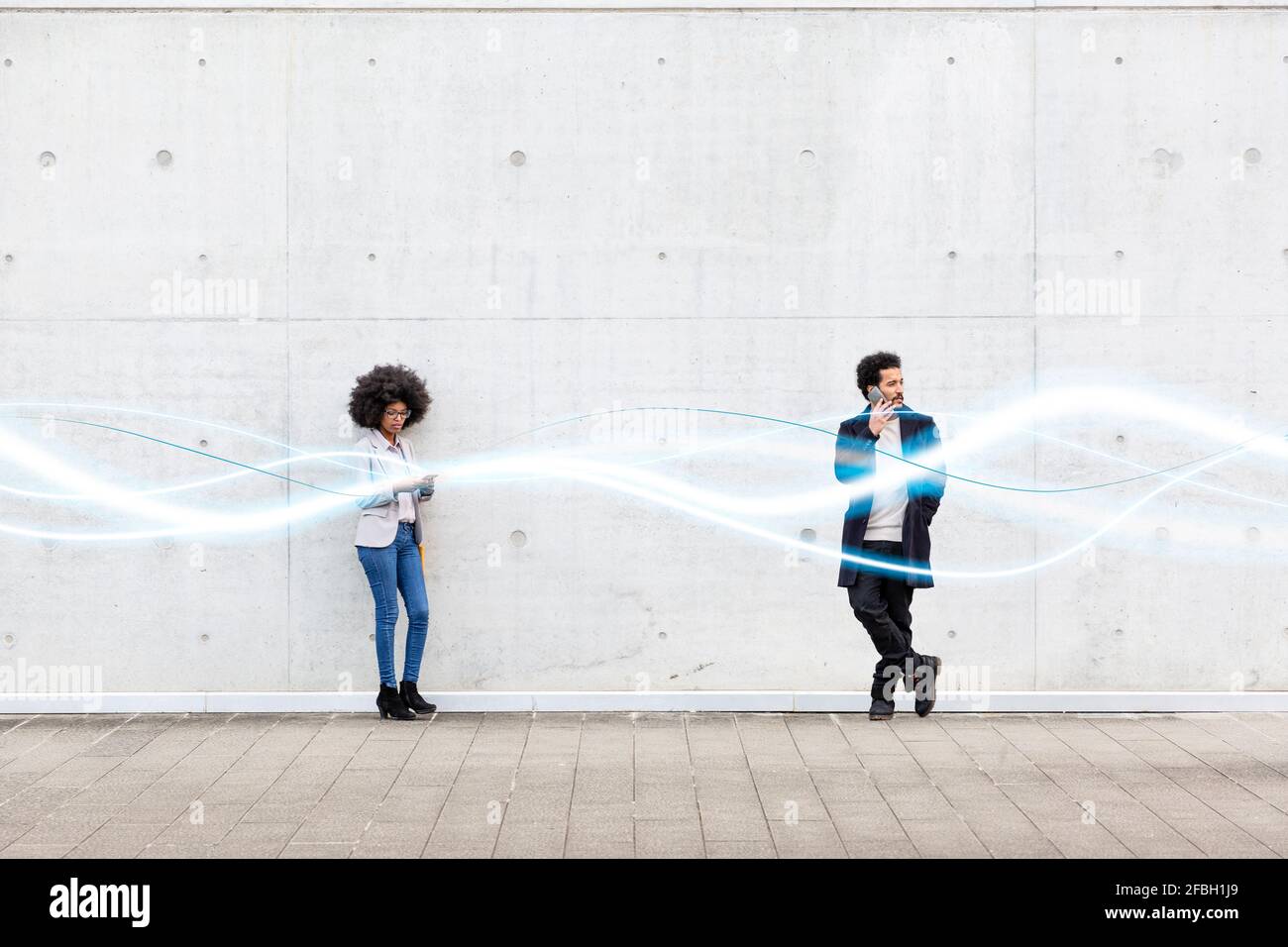 Businesswoman using mobile phone while standing by man with glowing wave pattern on footpath Stock Photo