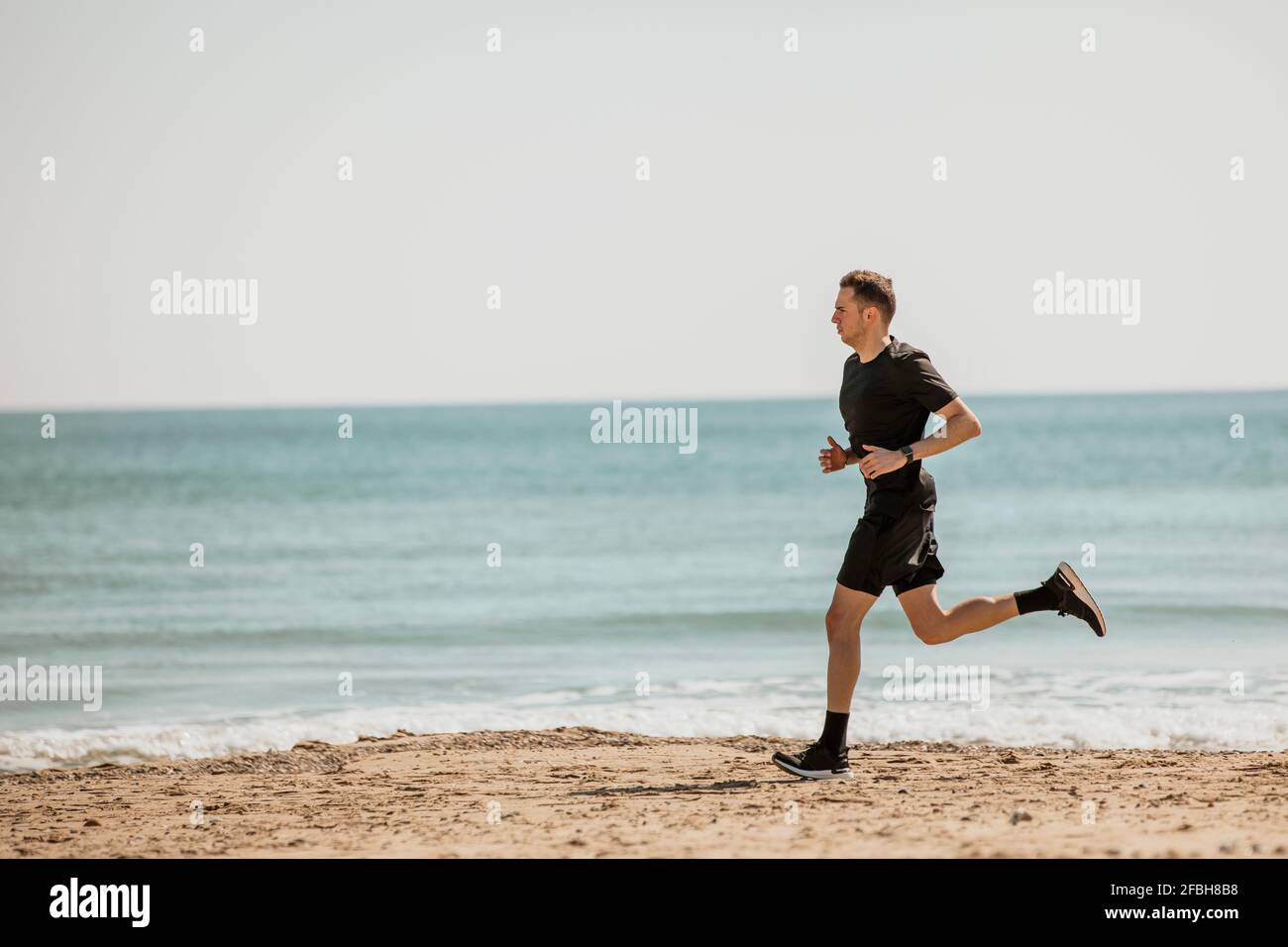 Young man running at beach during sunny day Stock Photo