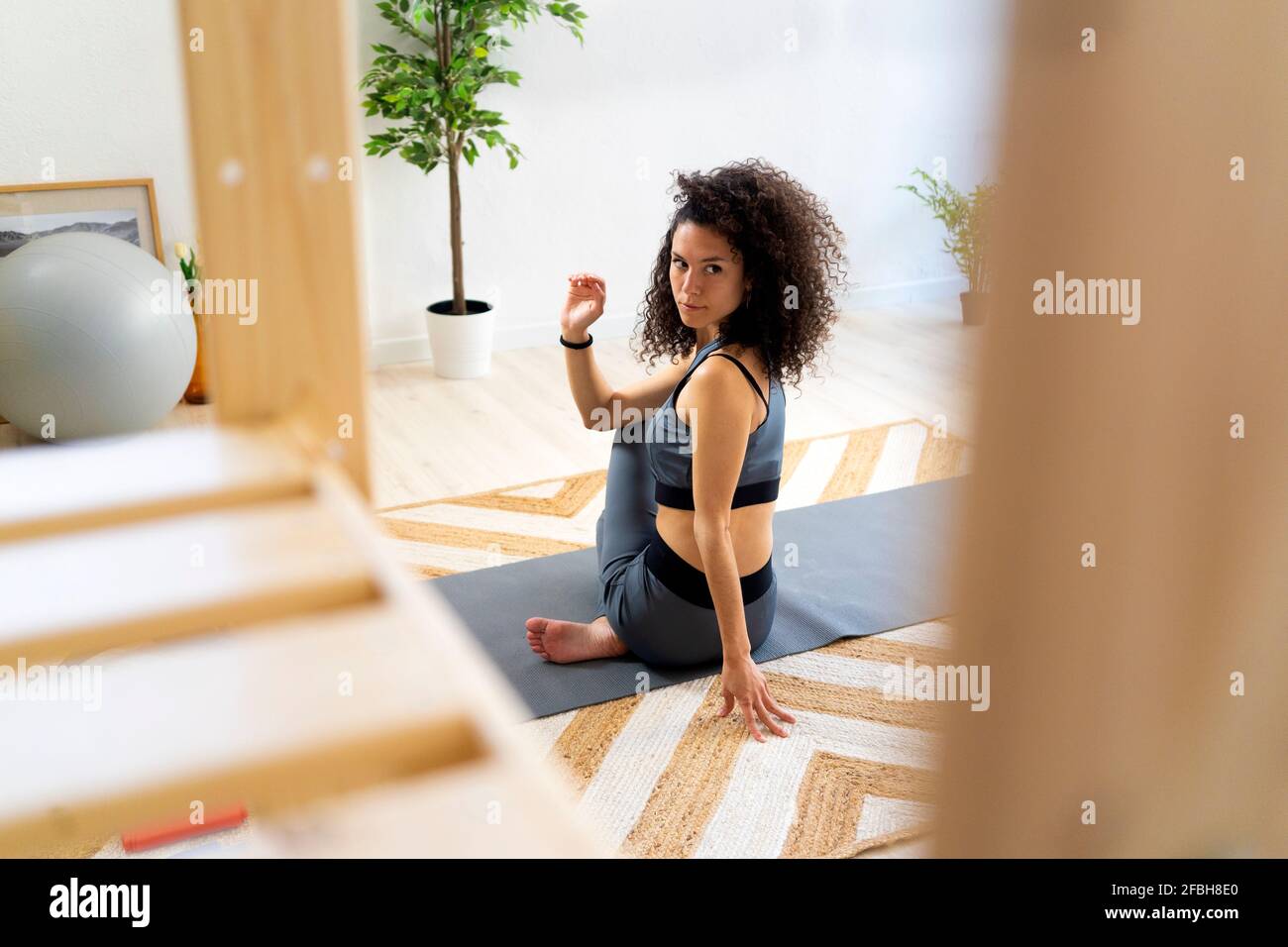 Woman with curly hair doing spinal twist pose at home Stock Photo