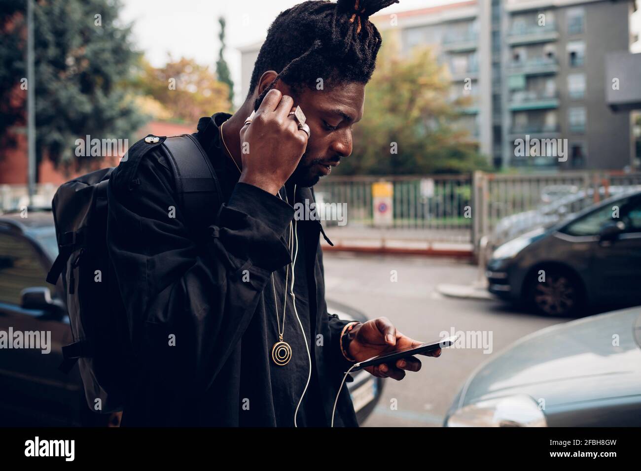 Man adjusting in-ear headphones while using mobile phone Stock Photo