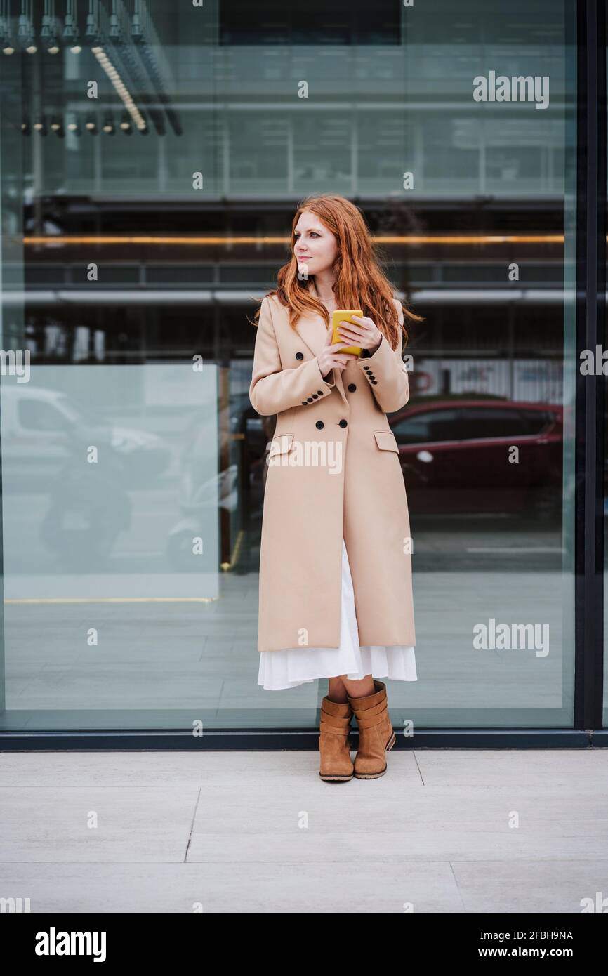 Woman in trench coat holding mobile phone on footpath Stock Photo - Alamy