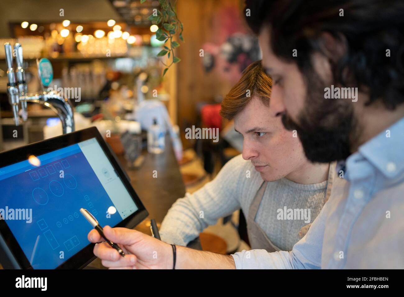 Businessman explaining table positioning to male colleague on restaurant computer Stock Photo